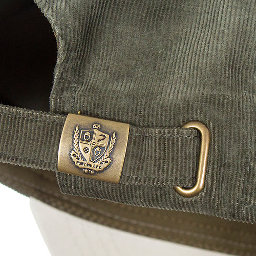 Close-up of an olive green corduroy hat with a brass metal buckle and a crest patch on the strap.